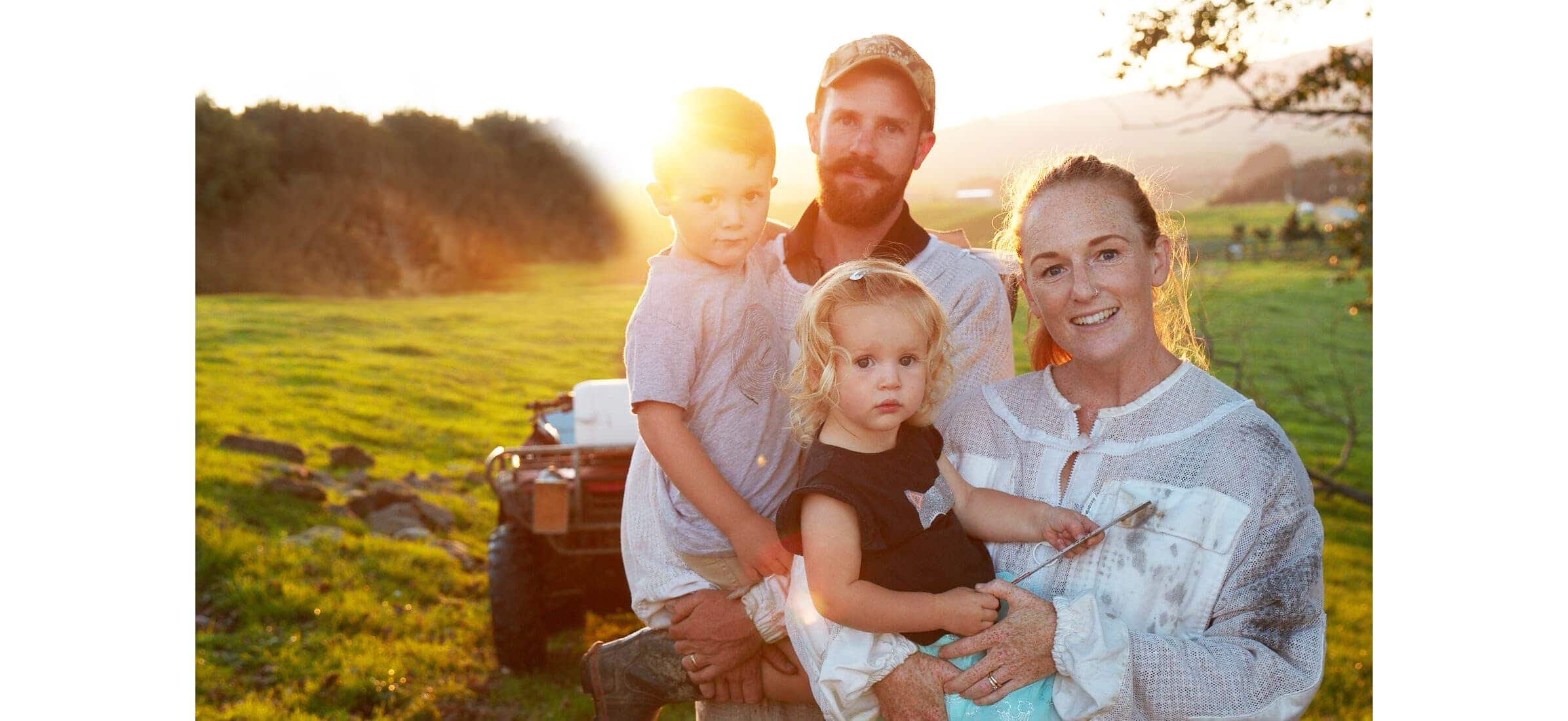 Rory and Hannah O’Brien with their two young children all smiling at the camera in a field at sunset.